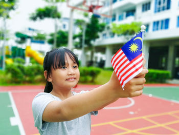 Smiling girl holding malaysian flag in park