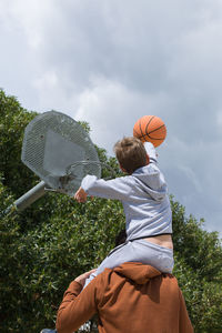 Rear view of boy holding umbrella against sky