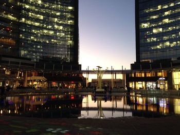 Illuminated buildings by river against sky at night