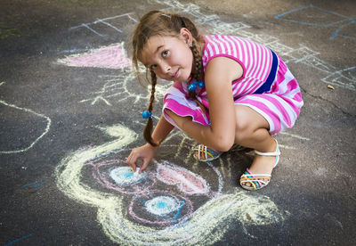 Smiling girl drawing with chalk on street