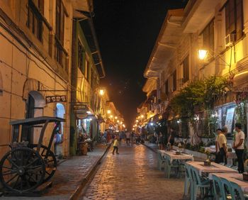 People on illuminated street amidst buildings in city at night