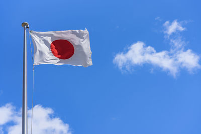 Japanese national flag waving in the wind against a sunny blue sky.