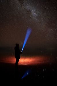 Silhouette of woman standing against illuminated flashlight against sky at night