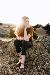 Woman sitting on rock against clear sky during sunset