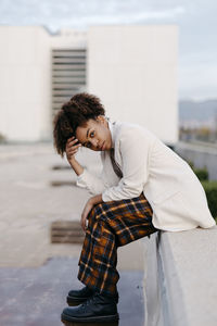Afro young woman with head in hands sitting on retaining wall against building