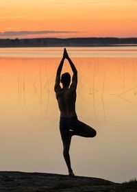 Rear view of silhouette man practicing tree pose at lakeshore