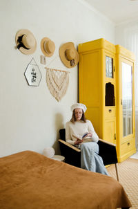 Young woman in beret sits in cozy home, room with music record in hands. vintage yellow cabinet.