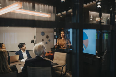 Businesswoman discussing ideas with male and female entrepreneurs during meeting in board room