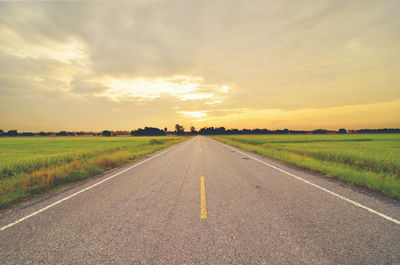 Road amidst field against sky during sunset