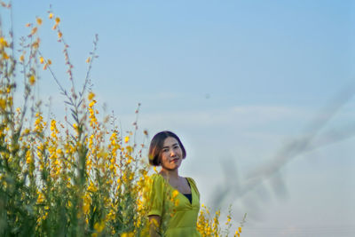 Woman standing on yellow flowering plants against sky