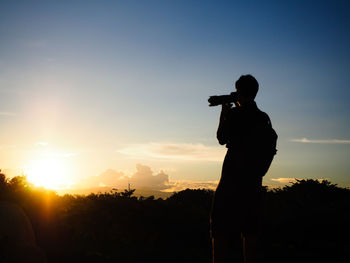 Silhouette man photographing against sky during sunset