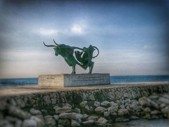 Statue by sea against sky