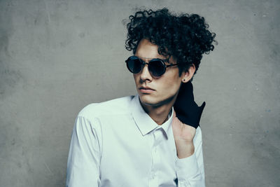 Portrait of young man wearing sunglasses standing against wall