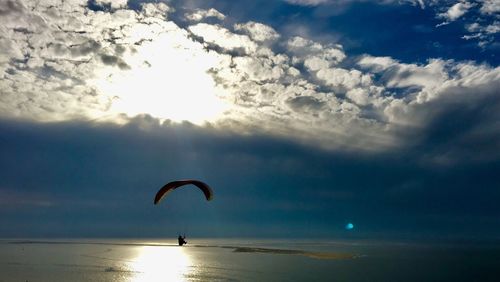 Silhouette flying person by sea against sky during sunset