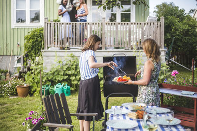 Mother and daughter preparing food on barbecue in backyard party