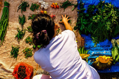 Rear view of vendor arranging vegetables on plastic sheet in market