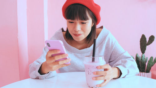 Young woman using mobile phone while having drink at table