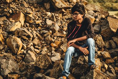 Young man looking away while sitting on rock