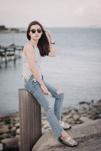 Young woman standing on rock at sea shore against sky