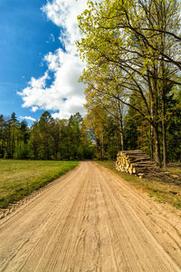 Dirt road amidst trees against sky