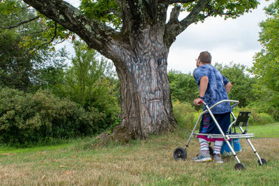 Disabled man walking with help of walker on grass against trees