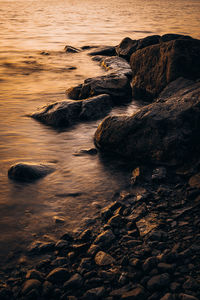 Rocks at sea shore against sky during sunset