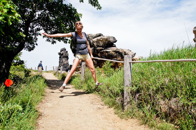 Smiling woman jumping on trail against sky