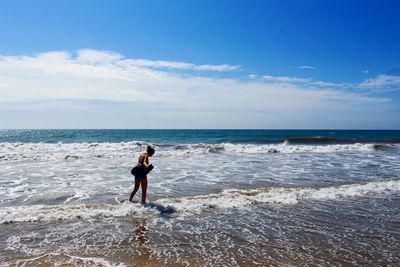 Woman walking on shore at beach against sky during sunny day