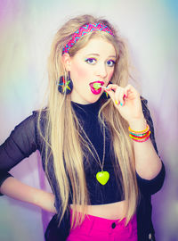 Portrait of young woman eating lollipop against wall