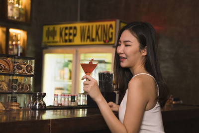 Woman holding glass while standing at bar