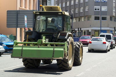 Tractor vehicle circulating on city street with farmer driving in rear view