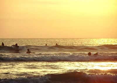 Silhouette people on beach against sky during sunset