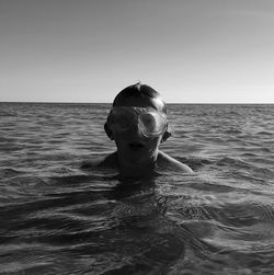 Portrait of boy in swimming goggles in sea against clear sky