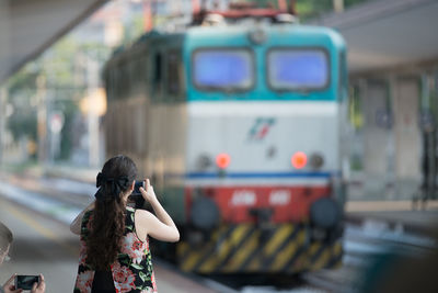 Rear view of woman photographing train at station