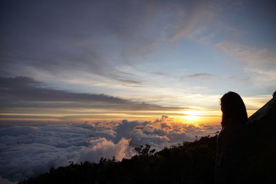 Silhouette woman standing on mountain against cloudscape during sunset