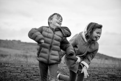 Happy siblings in warm clothing standing on field against sky