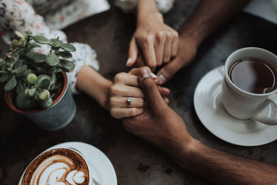 Cropped hand of man holding hands with woman by coffee at table