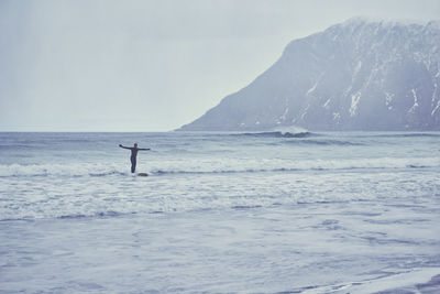 Man surfing on sea by snowcapped mountain against sky