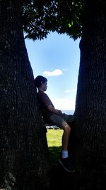 Boy sitting on tree trunk against sky