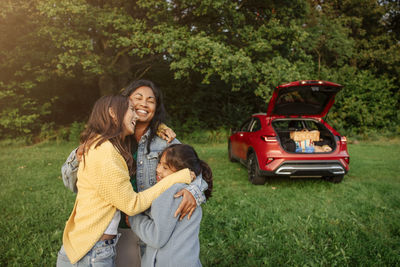 Smiling mother embracing daughters near car at park