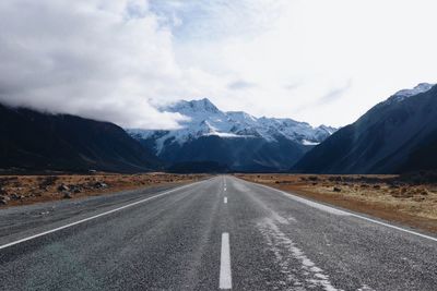 Empty road leading towards mountains against sky