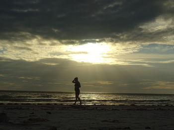 Silhouette man standing on beach against sky during sunset