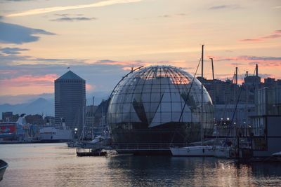 Sailboats in city by buildings against sky during sunset