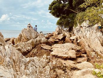 People on rocks by sea against sky