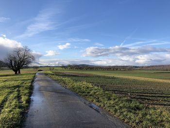 Empty road amidst field against sky