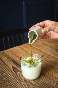 Midsection of person pouring drink in glass on table