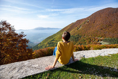 Young woman is sitting and looking at autumn landscape in italy. 