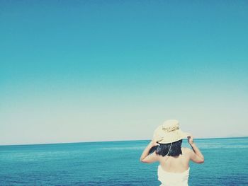 Rear view of woman by sea against clear blue sky