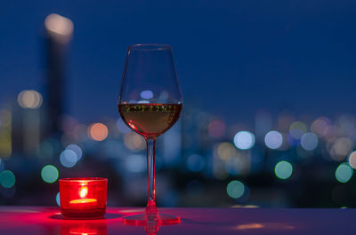 A glass of rose wine with red candle on table and colorful city bokeh light background.