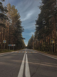 Empty road by trees against sky in city